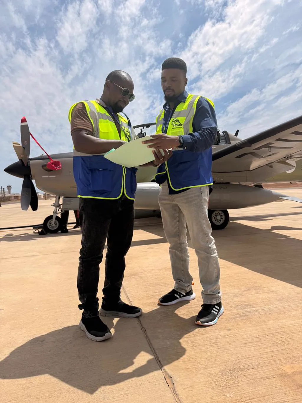 Two Flysafe supervisors reviewing handling paperwork beside a turboprop aircraft